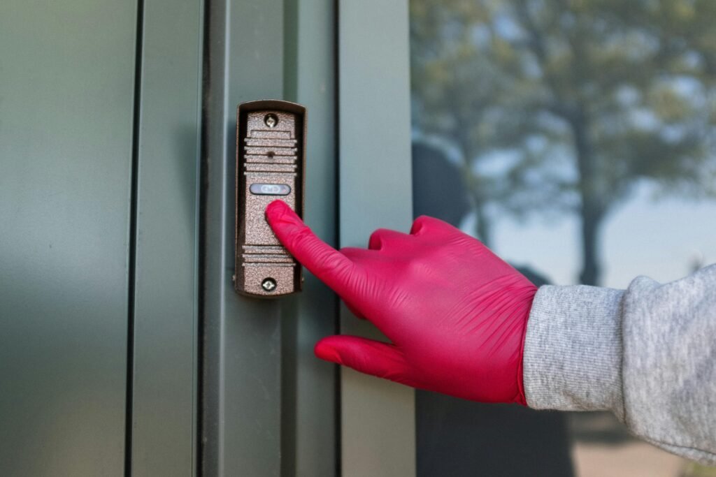 A red gloved hand presses a modern doorbell on a metal door, depicting security and service.