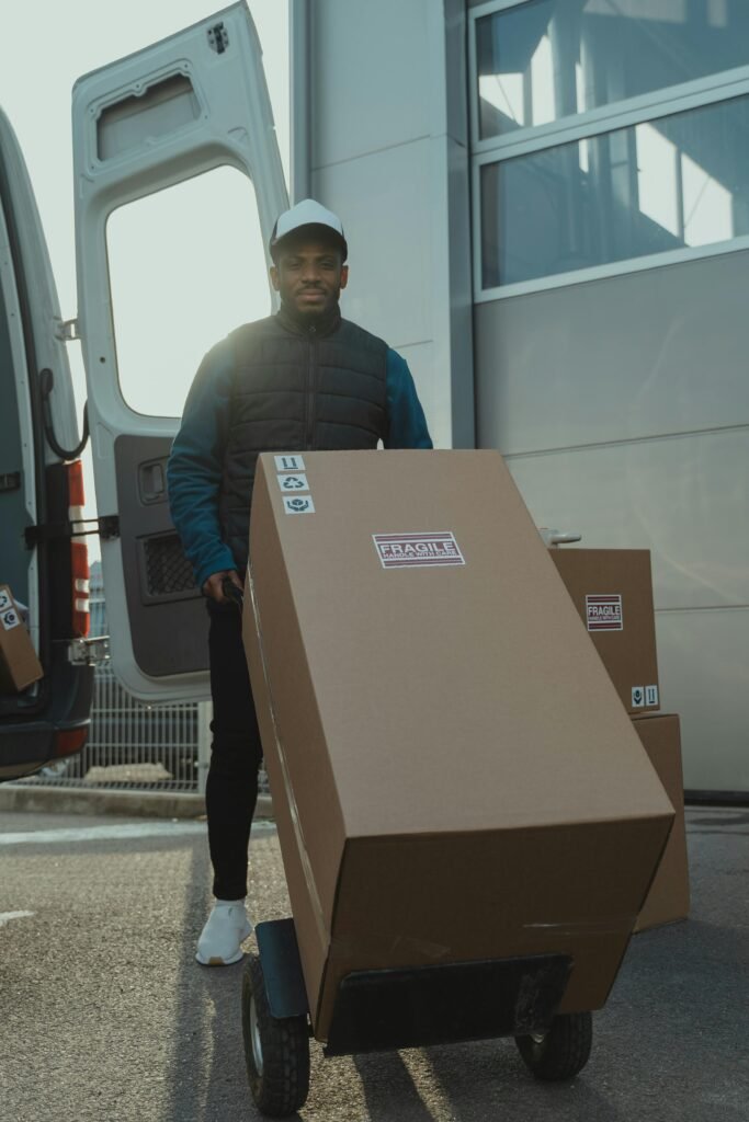 A delivery man moving cardboard boxes with a trolley outside in daylight.